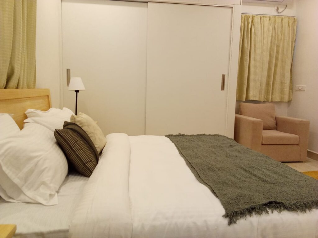 Modern hotel room with a comfortable double bed, wardrobe, bedside lamp and seating area.