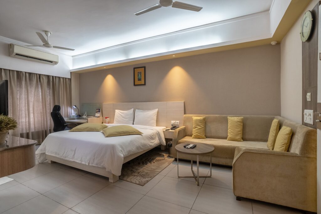 Comfortable hotel room at Enkay Nemrana featuring a king-size bed, beige sofa, modern interiors, and warm lighting.